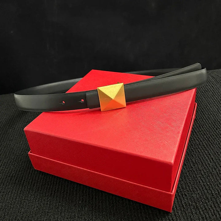 A leather belt with a large gold buckle and adjustable length rests on a closed, textured red box against a black background.
