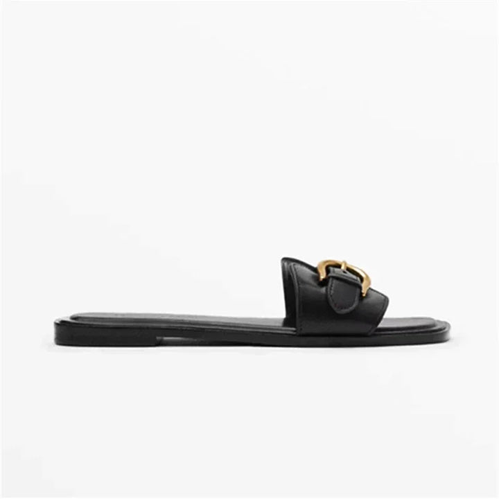 A black leather slide sandal with an open toe and a gold buckle detail on the strap, shown in a side profile view against a plain white background for an easy slip-on style.