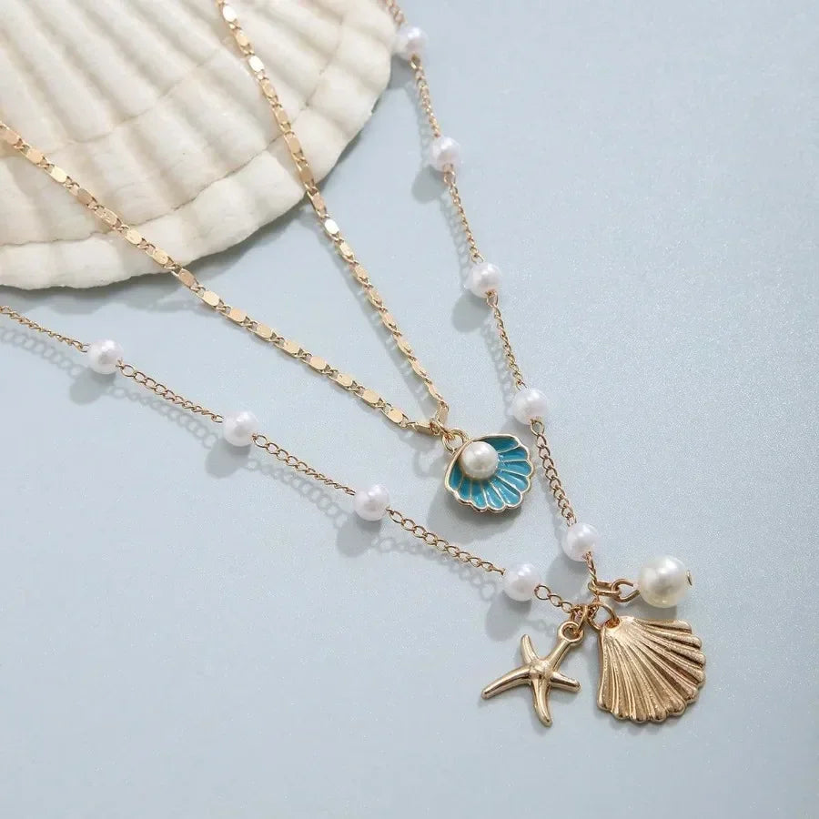 Layered gold necklace with pearl, shell, and starfish charms on a light background, Rovelli