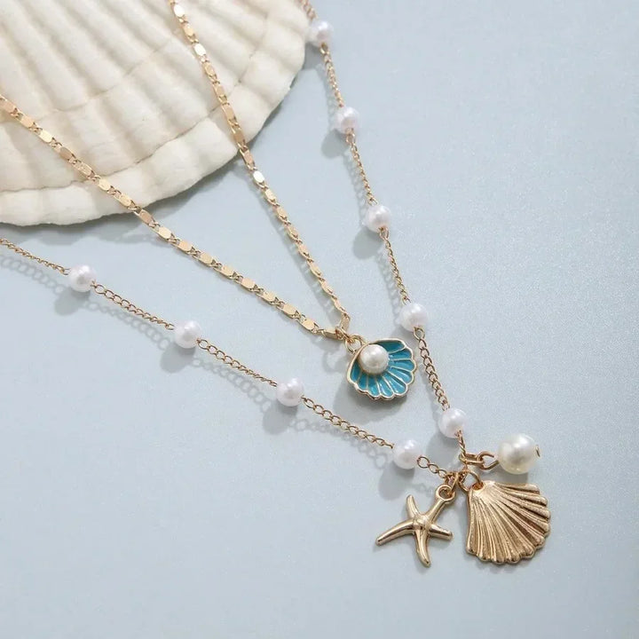 Layered gold necklace with pearl, shell, and starfish charms on a light background, Rovelli