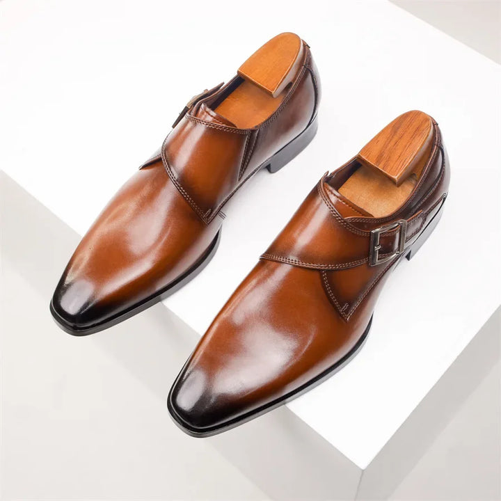 A pair of polished Italian leather monk strap shoes with wooden shoe trees inside, displayed on a white surface.