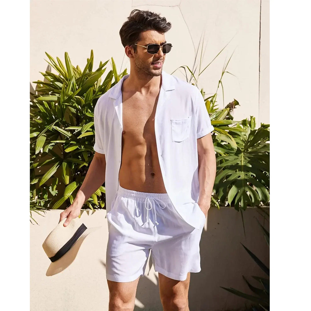 Man wearing white short-sleeve button shirt and shorts, holding hat, outdoor summer fashion by Rovelli