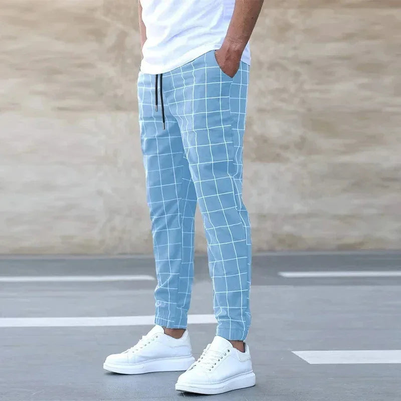 Man wearing Rovelli blue grid jogger pants and white sneakers, standing outdoors