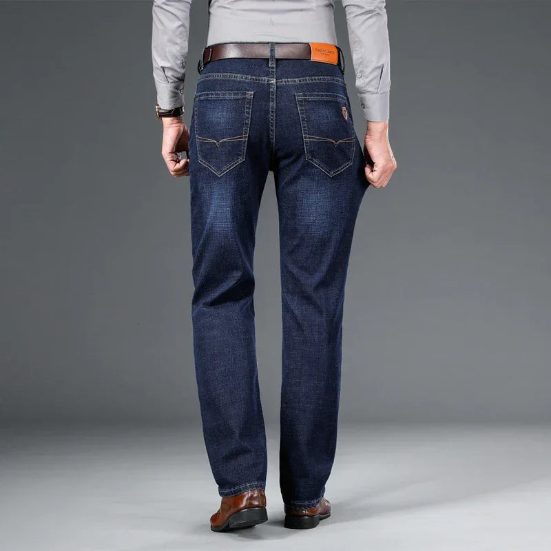 Man wearing dark blue Rovelli jeans, brown belt, grey shirt, and brown shoes, back view