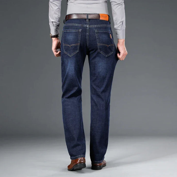Man wearing dark blue Rovelli jeans, brown belt, grey shirt, and brown shoes, back view
