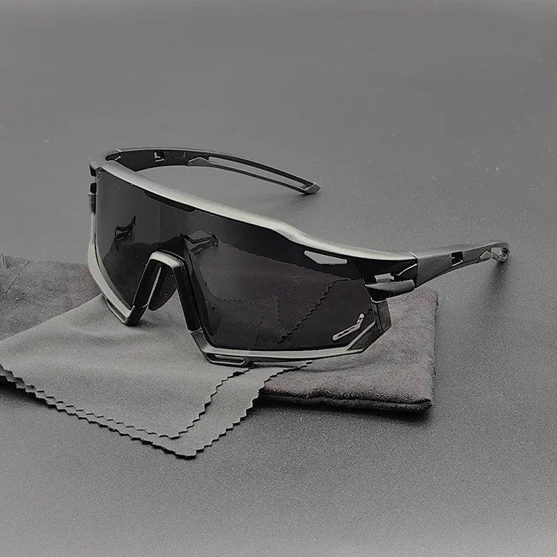 A pair of modern, angular black Olympus Sunglasses with polarized lenses and dark shades rests on two soft cleaning cloths atop a gray surface.