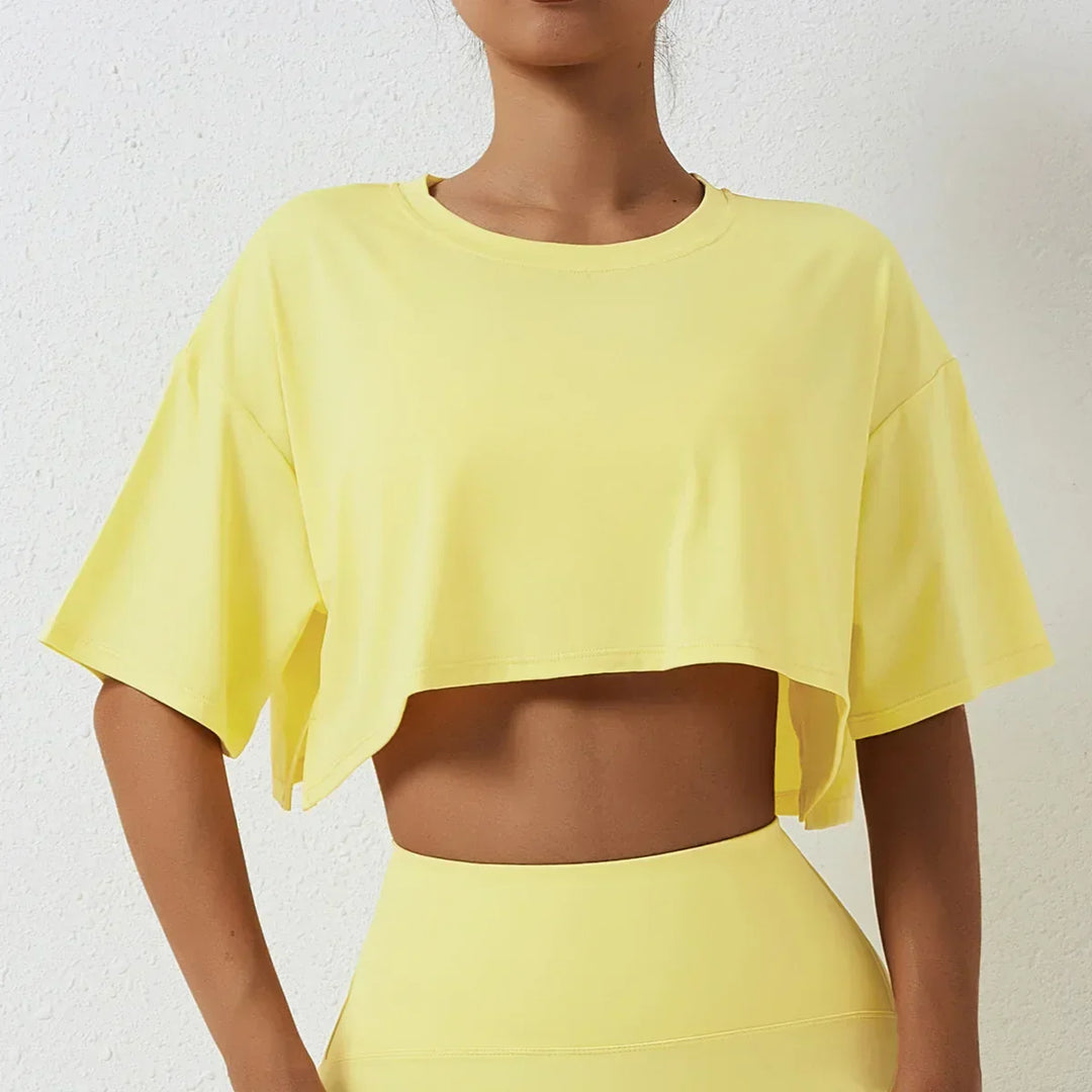 A woman in a relaxed fit, cotton crop top and matching high-rise pants stands against a light textured wall. Her face is partially out of the frame.