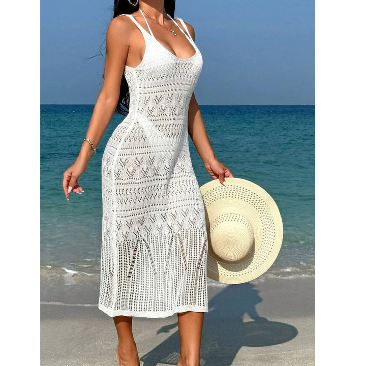 Woman wearing white crochet beach dress and holding straw hat by the ocean, Rovelli fashion