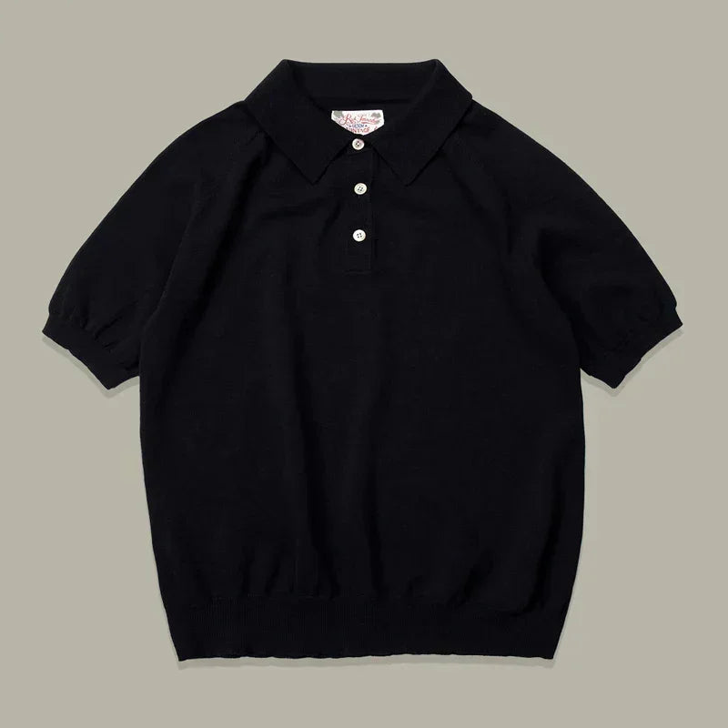 A classic style polo, this short-sleeve black knit mens polo shirt features a collar, three white buttons, ribbed cuffs, and a ribbed hem, laid flat on a neutral background.