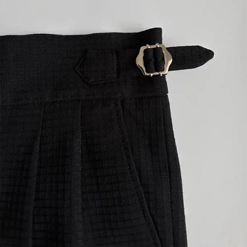 Close-up of the waistband of black luxury tailored pants with a silver buckle and strap detail on the side, set against a light background.
