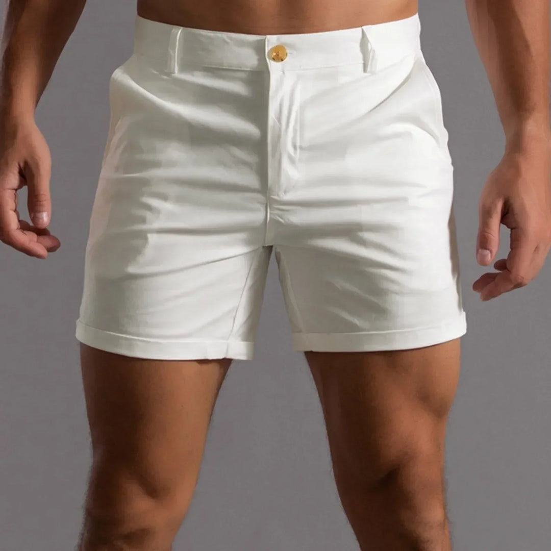 A person stands against a gray background, wearing white fitted shorts with a semi elastic waistband and tailored fit; torso and legs are visible, but the persons face is not shown.
