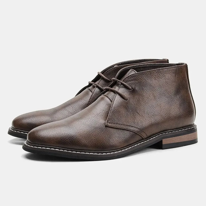 A pair of brown leather boots, the After-Ride Chukka, feature a textured finish, low heels, and black rubber soles with white stitching detail, displayed on a white background.