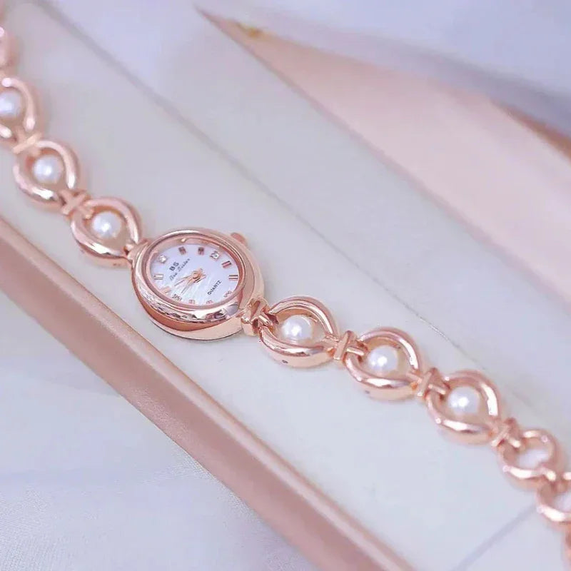 A rose gold wristwatch with a delicate bracelet design and pearl accents, featuring precision quartz movement, displayed inside a light-colored jewelry box.
