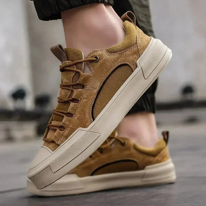 Close-up of a person wearing stylish brown suede canvas shoes with beige soles, standing on a pavement. The sneakers feature textured panels, cushioned insoles, and thick, durable rubber outsoles for added comfort and support.
