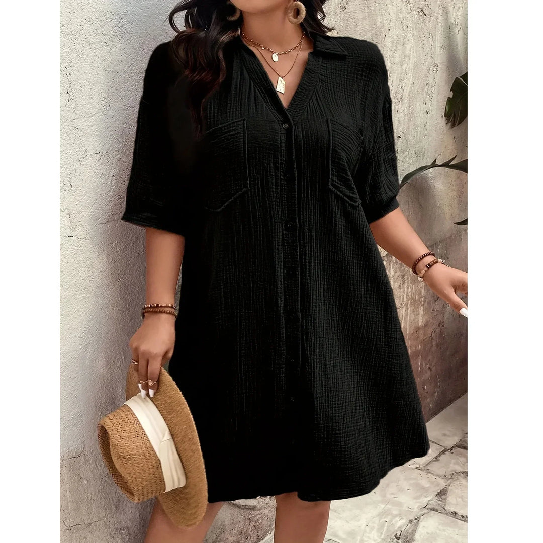 Woman wearing a black short-sleeve button-up dress from Rovelli, holding a straw hat