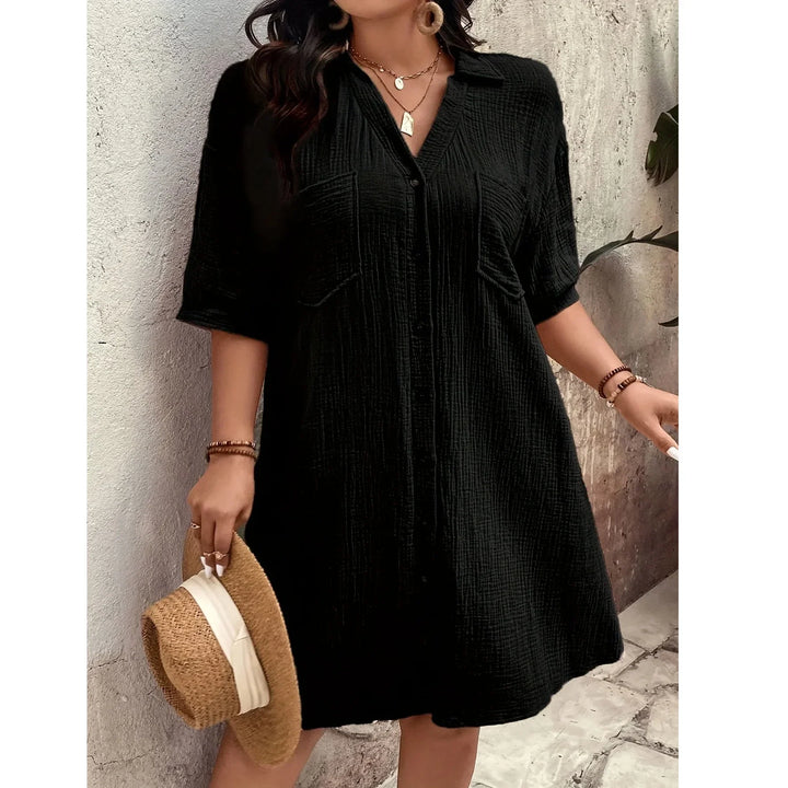 Woman wearing a black short-sleeve button-up dress from Rovelli, holding a straw hat