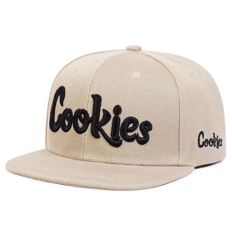 A beige flat-brim hat made from breathable fabric, featuring the word Cookies embroidered in large black script on the front and smaller on the side. An adjustable strap ensures a comfortable fit.
