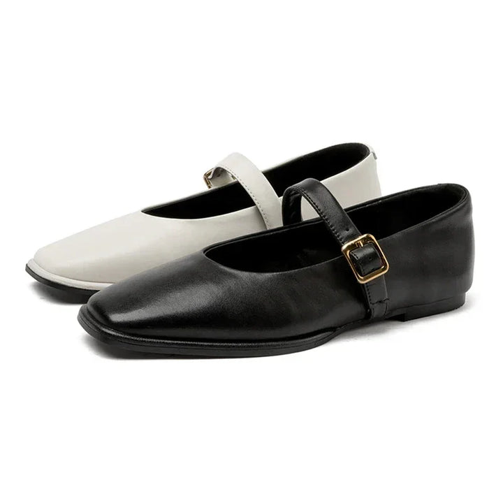 A pair of Mary Jane shoes; one is black and the other white, each with a thin strap and small gold buckle. These elegant ballet flats for ladies are displayed on a plain white background, highlighting their simple charm.