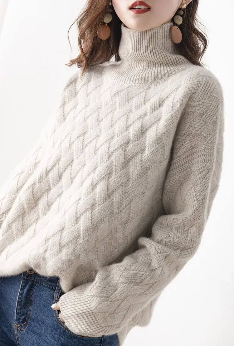 A woman wears a cream-colored, ultra soft cable knit turtleneck sweater with blue jeans. She has medium-length brown hair, statement earrings, and poses against a plain white background.