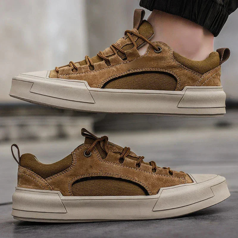 A pair of brown suede canvas shoes with white durable rubber outsoles. One shoe is worn and slightly lifted, while the other rests flat on a gray surface. The shoes feature brown laces and casual, sporty styling.