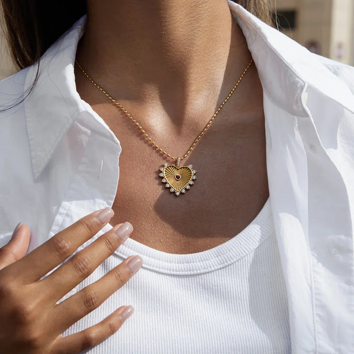 Woman wearing gold heart pendant necklace with gemstones, styled with a white shirt, Rovelli jewelry