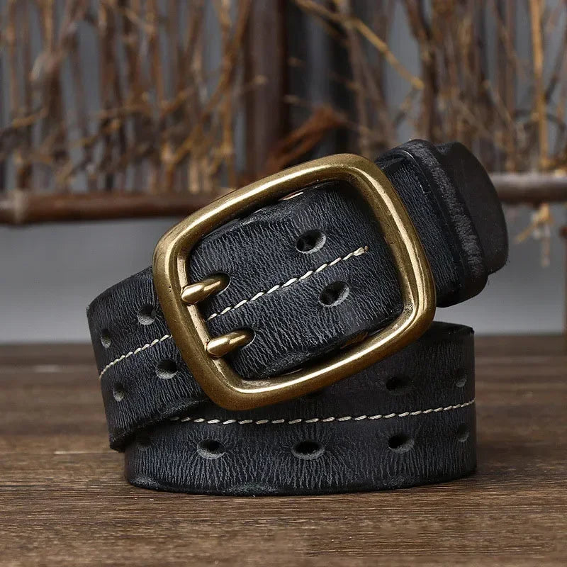 A genuine leather belt with white stitching, multiple oval holes, and a large, square, copper buckle is coiled on a wooden surface with a blurred rustic background.