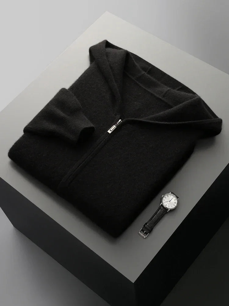 A neatly folded black men wool cardigan and a black leather-strapped wristwatch with a white face are displayed on a square, light gray surface against a neutral background.