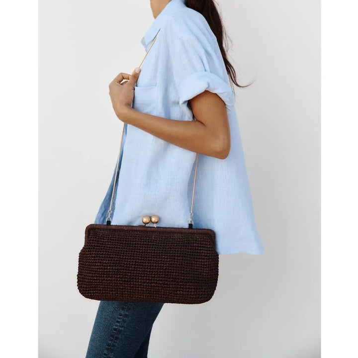 Woman in light blue shirt holding Rovelli dark brown woven shoulder bag with gold clasp