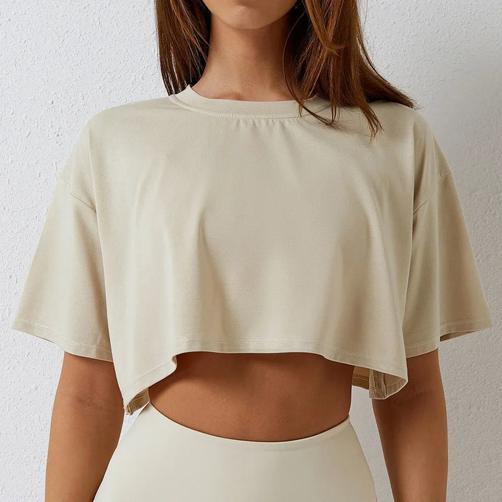 Woman wearing a loose, short-sleeved cotton crop top and matching high-rise pants stands against a light textured wall. Her face is partially out of frame, highlighting the relaxed fit of her outfit.