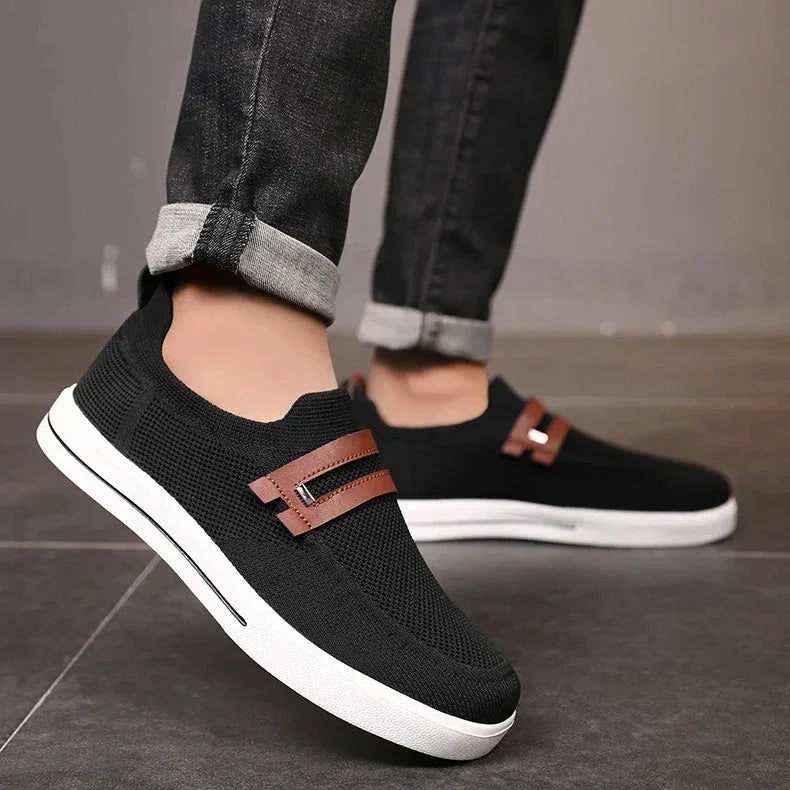 Rovelli black slip-on sneakers with brown accents and white soles, worn with rolled jeans