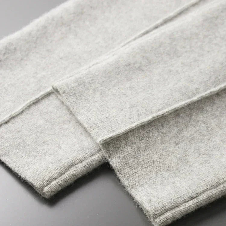 Close-up of two pieces of light gray, soft, felted fabric—perfect for Merino wool pants—with visible stitched edges, laid flat and overlapping on a smooth, dark surface, hinting at comfortable pants with durable construction.
