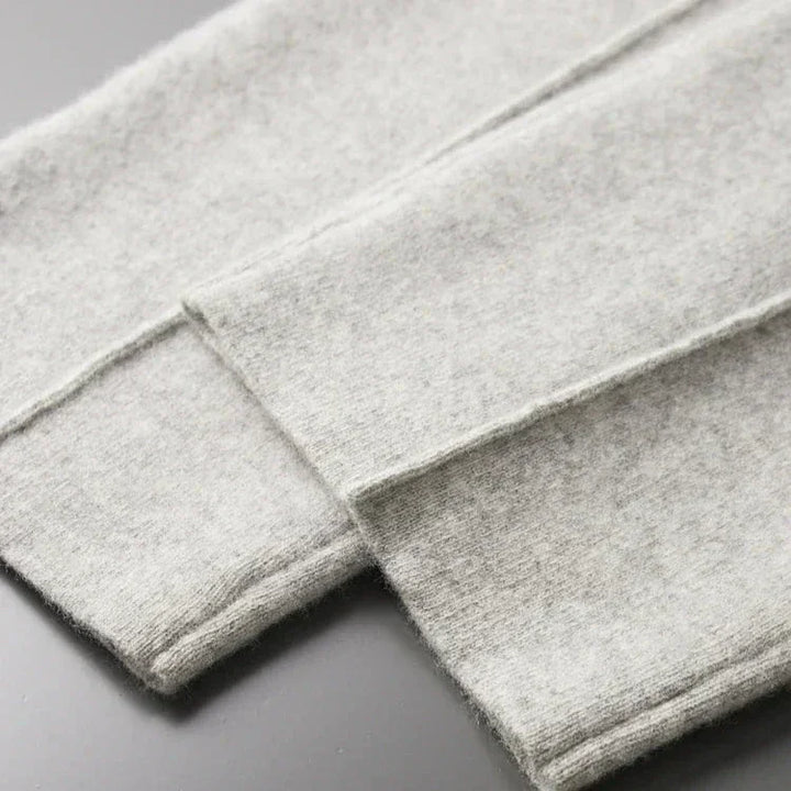 Close-up of two pieces of light gray, soft, felted fabric—perfect for Merino wool pants—with visible stitched edges, laid flat and overlapping on a smooth, dark surface, hinting at comfortable pants with durable construction.