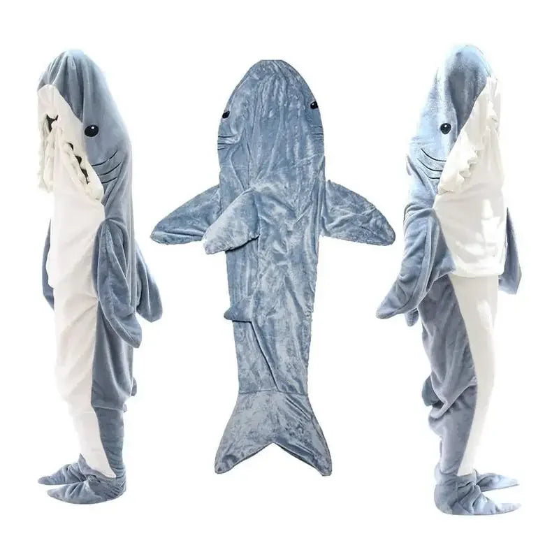 Three views of a person wearing a full-body, plush shark costume: front, back, and side. The suit resembles cozy pajamas in gray and white with fins, a tail, and a shark face with teeth around the hood.