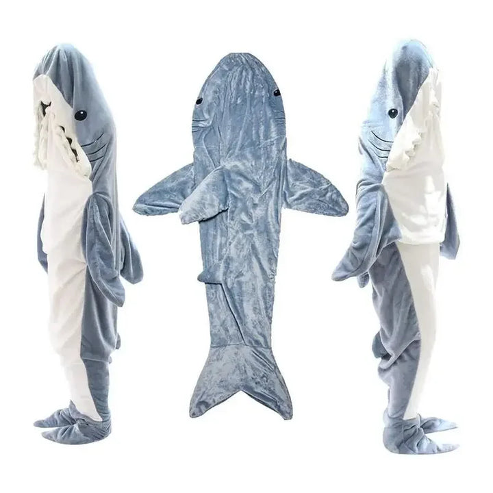 Three views of a person wearing a full-body, plush shark costume: front, back, and side. The suit resembles cozy pajamas in gray and white with fins, a tail, and a shark face with teeth around the hood.