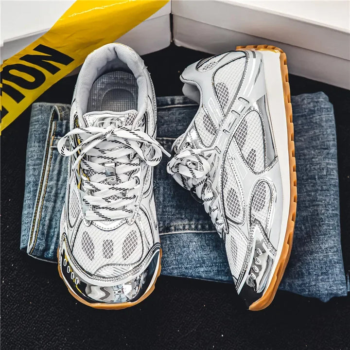 A pair of white and silver sneakers with a cushioned insole and gum soles are placed on folded blue jeans. A yellow CAUTION tape and white boxes are partially visible in the background.