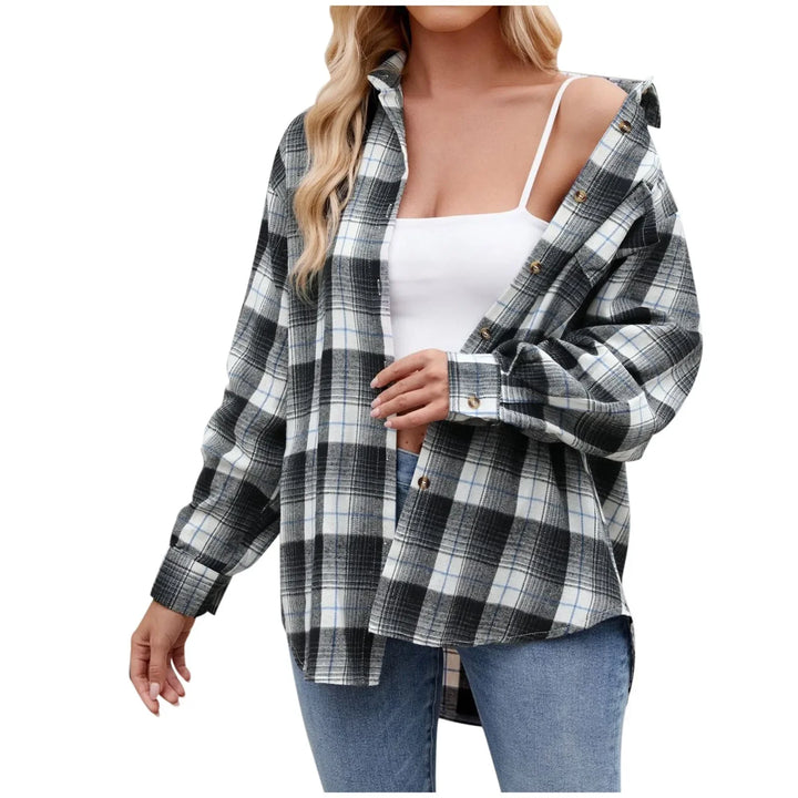 A woman wears an oversized fit black and white plaid button-down shirt over a white tank top and blue jeans, with the shirt partially unbuttoned for effortless layering. Her hair is down against a plain white background.