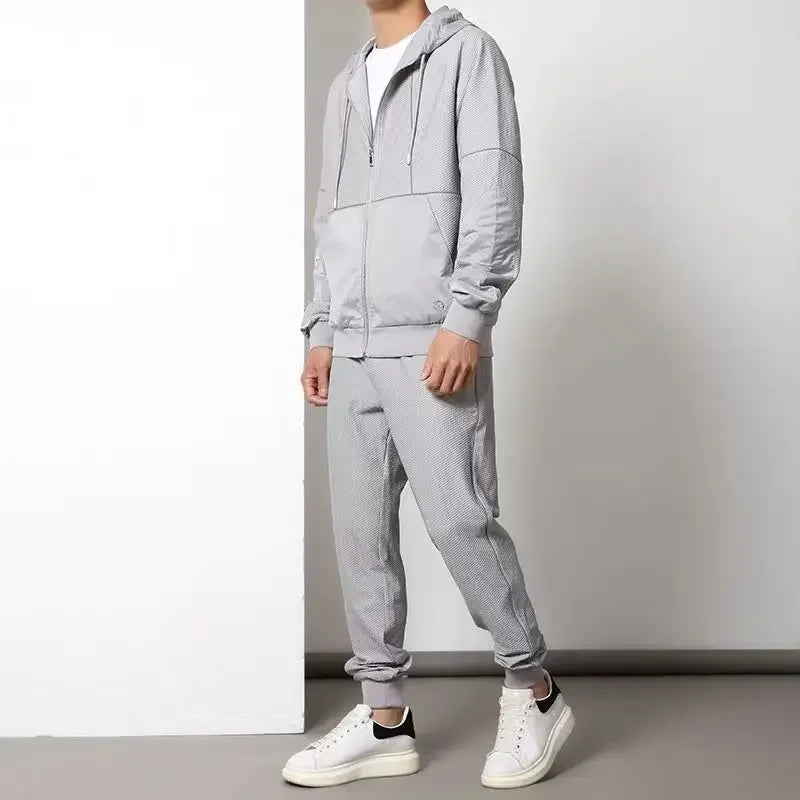 A person wearing a light gray activewear set, featuring a moisture wicking zipper hoodie and matching jogger pants with white sneakers, stands against a plain white and gray background. The persons face is not visible.