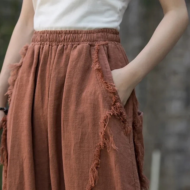 Woman wearing high-waisted, brown frayed wide-leg pants from Rovelli, hand in pocket