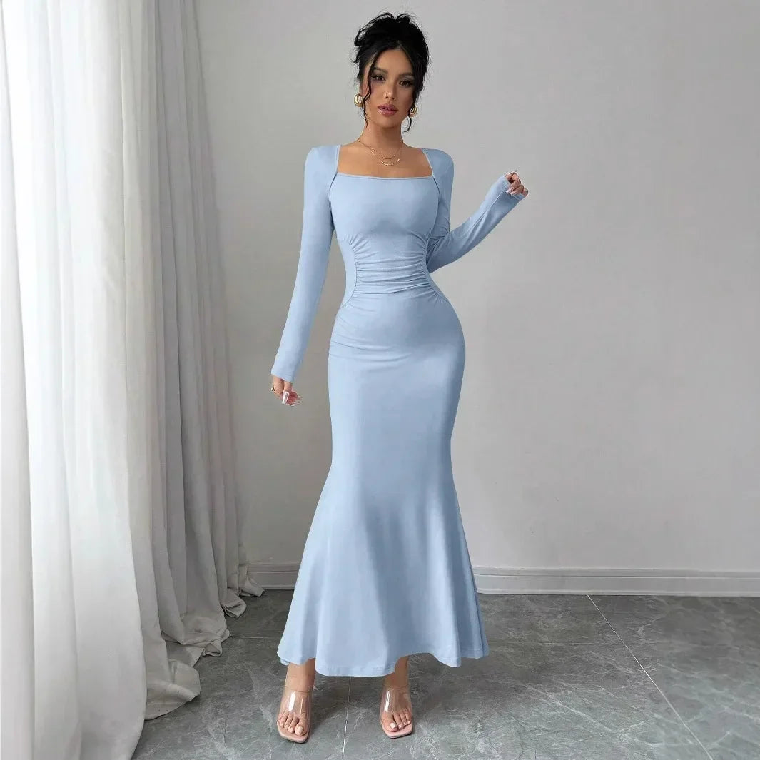 Woman wearing light blue long sleeve fitted maxi dress from Rovelli, standing indoors on gray tile