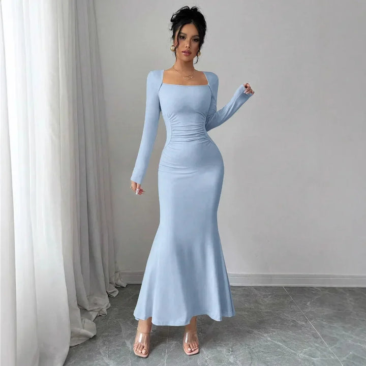 Woman wearing light blue long sleeve fitted maxi dress from Rovelli, standing indoors on gray tile