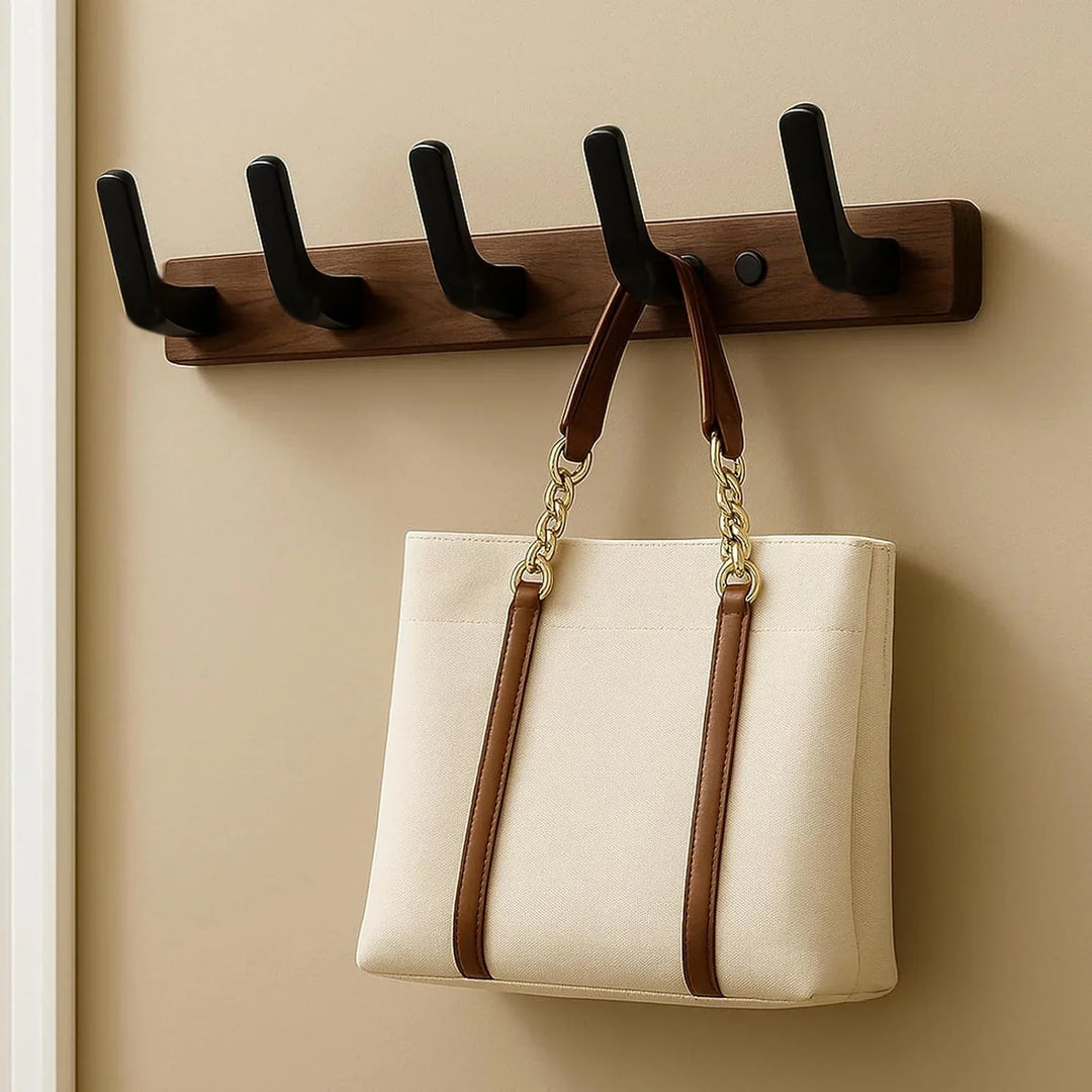 Wooden wall coat rack with four black hooks, holding a beige tote bag with brown straps