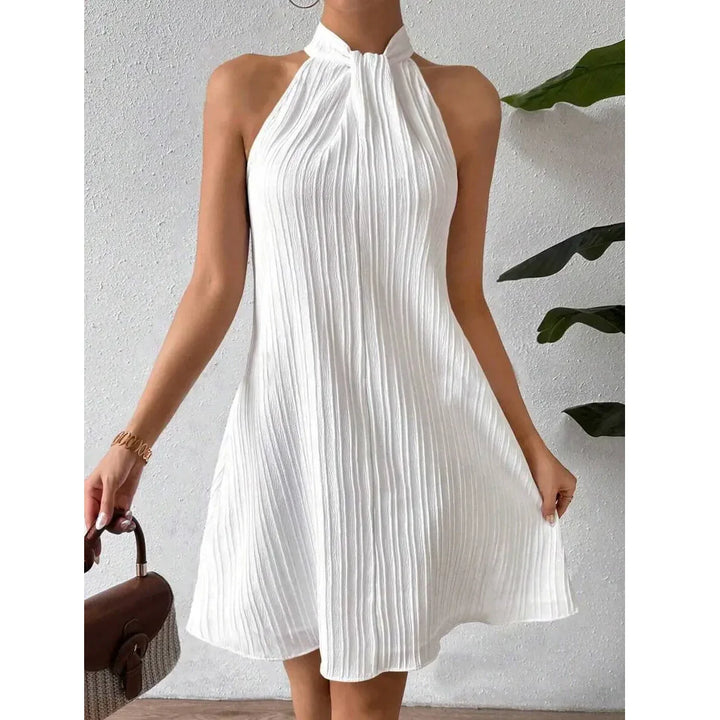Sleeveless white pleated halter dress from Rovelli against a white textured wall