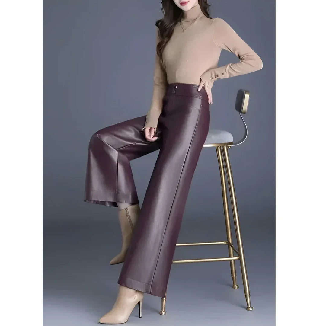 Woman in beige turtleneck and burgundy wide-leg leather pants sitting on gold chair, Rovelli fashion