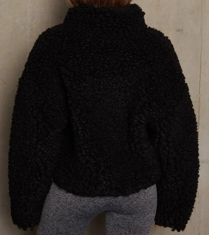 A person wearing a black jacket with a full zip closure and a bulky cropped fit.