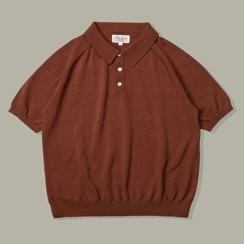 A short-sleeved brown organic cotton polo with a ribbed hem and sleeves, three white buttons, and a classic collar, laid flat on a neutral gray background.