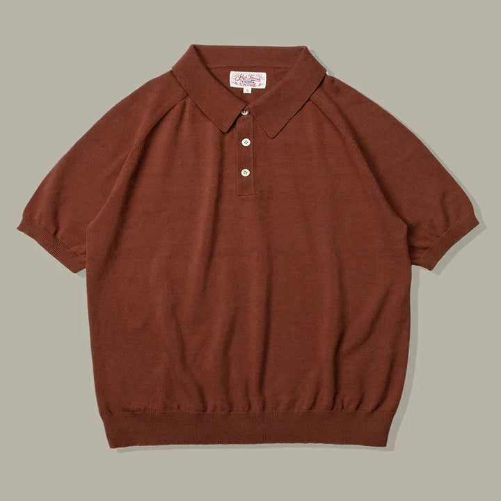 A short-sleeved brown organic cotton polo with a ribbed hem and sleeves, three white buttons, and a classic collar, laid flat on a neutral gray background.