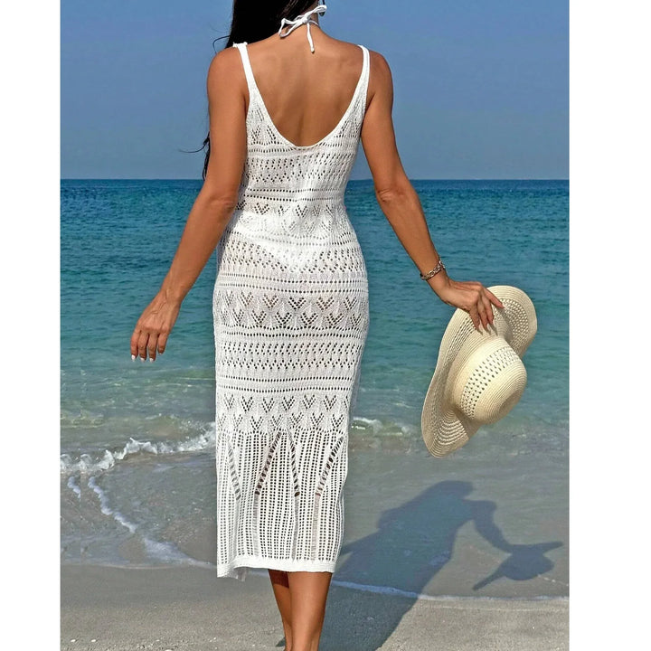 Woman in white crochet beach dress holding straw hat by ocean, Rovelli summer fashion