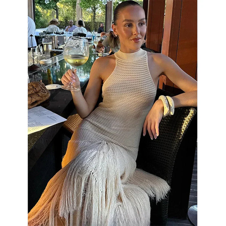 Woman in cream knit fringe dress holding wine glass, seated at outdoor restaurant table