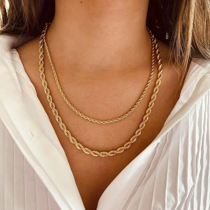 A woman wearing a white, pleated, v-neck blouse displays two layered gold rope chain necklaces crafted from non-fading materials around her neck.