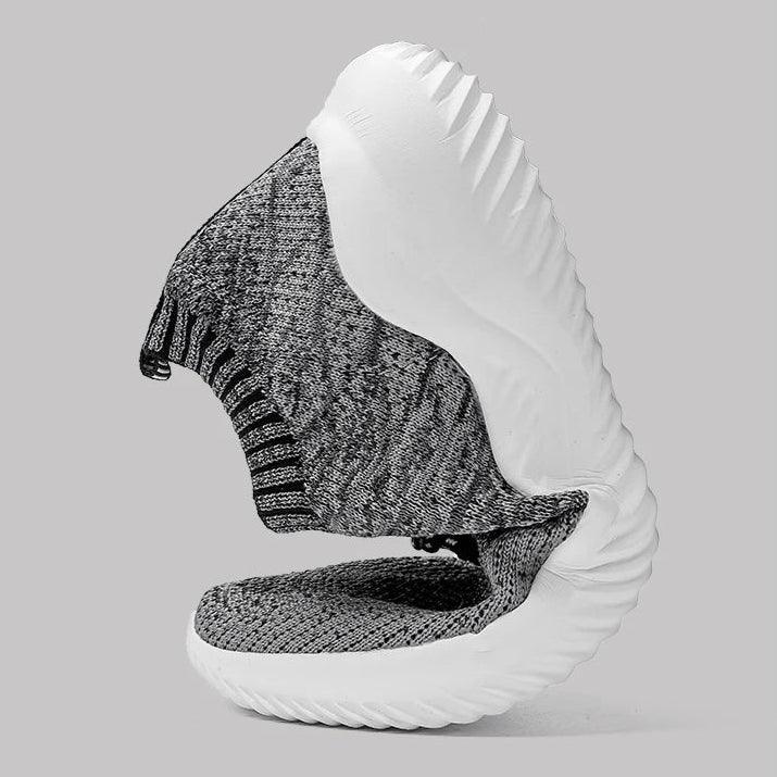 Flexible knit gray sneaker with thick white sole bending in half, Rovelli shoe on gray background
